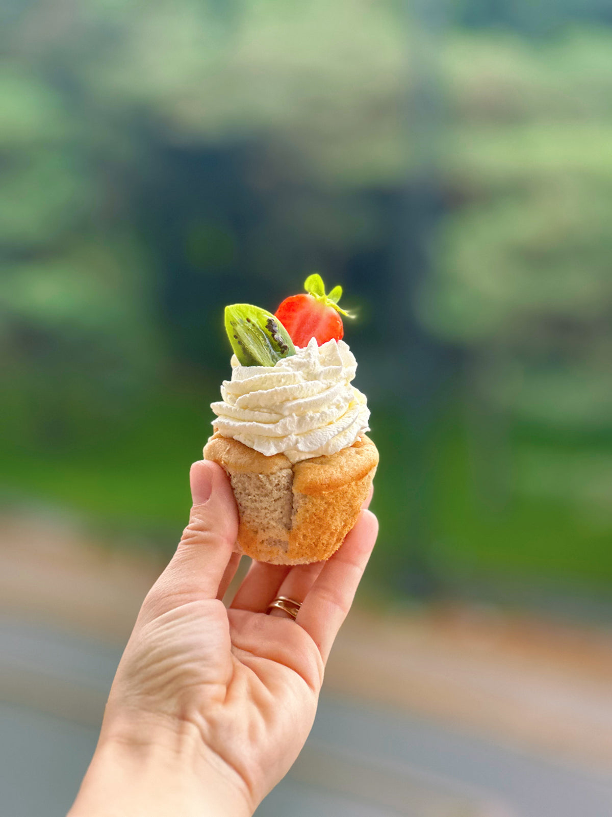 Gluten-free banana muffin with mascarpone frosting and fresh strawberry, held by hand
